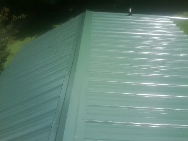 New green metal panels meeting at the ridge of a roof — Flat Roof Repair work by our crew in Lamar