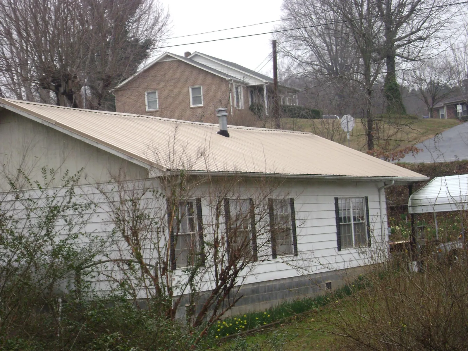 Tan metal roof on a white sided house set into a hillside — Commercial Roofing by Roofing Brothers in Lamar